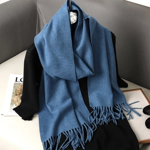 Detail view of a soft blue cashmere-feel scarf with fringe, paired with a camellia brooch