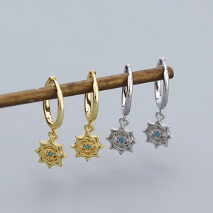 Detail of silver and gold evil eye star earrings with blue zircon insets on wooden support