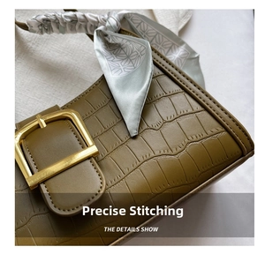 Close-up of olive green crocodile texture handbag with gold buckle and silk scarf detail