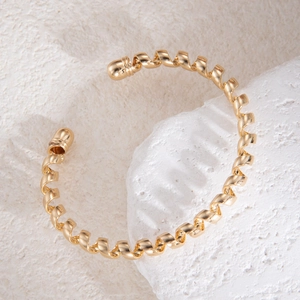 Détail macro d'un bracelet jonc torsadé doré posé sur une pierre texturée beige