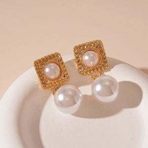 Macro shot of gold vintage square pearl earrings on a white stone display stand