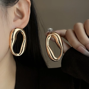 Detail shot of a large polished gold irregular oval earring worn by a model