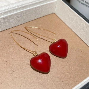 Macro detail of glossy red heart pendant with elegant long golden hook earrings