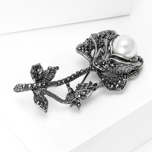 Macro shot of vintage rose brooch with pearl center and dark rhinestones on a white pedestal