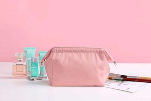 Pink waterproof travel makeup bag organized with cosmetics and perfumes on a stylish background