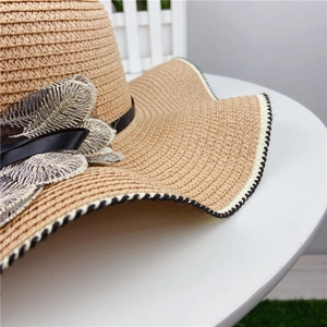 Detail of hand-woven straw hat featuring 3D leaf embroidery and black satin bow accent