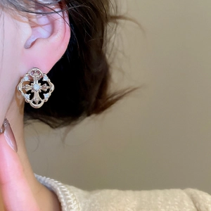 Close-up of golden hollow cross earrings with sparkling zircons worn by a model