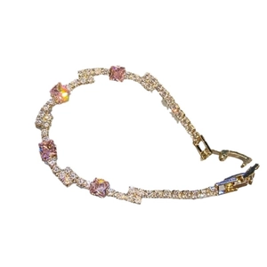 Elegant gold bracelet with square pink stones and white crystals on white backdrop