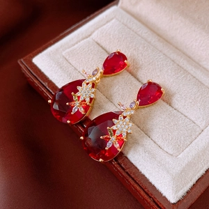 Macro shot of red waterdrop gems and golden flower zircon studs in a jewelry box