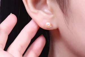 Detail shot of natural pink pearl earrings with shimmering zircon and gold base on ear