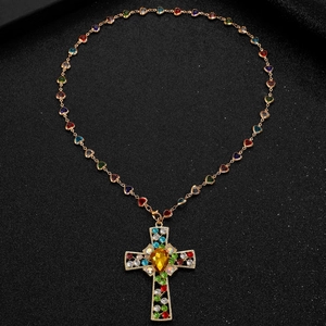 Macro detail of golden cross necklace pendant with colorful gemstones on black background