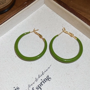 Detail of green enamel twisted earrings in a wooden tray with aesthetic props