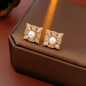 Macro detail of a square gold stud earring with a central pearl and zircon halo