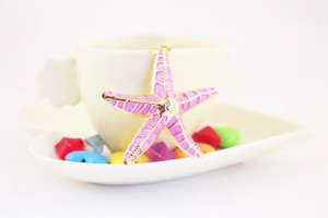 Detailed macro shot of a purple starfish keychain pendant with gold trim against a white cup