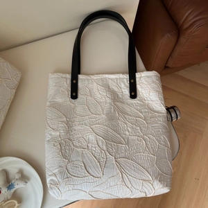 Detailed embroidery texture on a white canvas tote bag with black leather handles