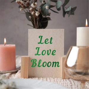 Close-up of a natural wood card holder with a Let Love Bloom glitter greeting card