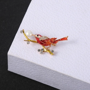 Close-up of golden bird brooch with red enamel wings, rhinestones and a white pearl