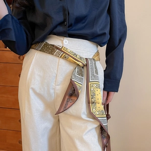 Detail of paisley print silk scarf used as a waist accessory on cream trousers