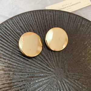 Gros plan de boucles d'oreilles rondes dorées polies sur un plateau noir texturé