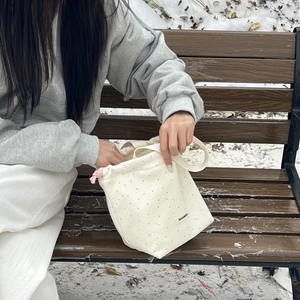 Detail of wool beige polka dot drawstring handbag with pink straps in a winter park setting