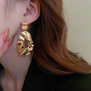 Macro detail of irregular gold geometric hoop earrings with textured wrinkle finish
