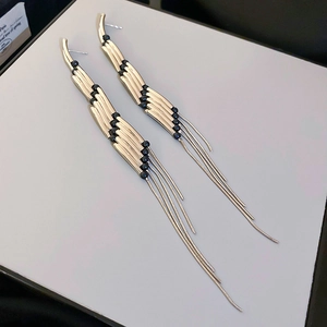 Detail of long gold metal and black bead tassel earrings in a modern minimalist style