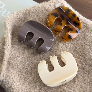 Three acrylic hair claws in amber, taupe, and cream beige on a soft faux fur background
