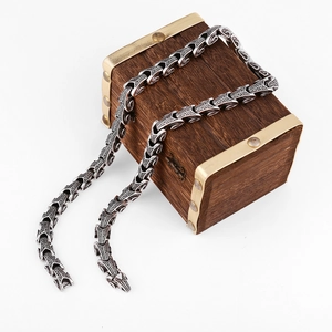 Detail of vintage steel dragon chain necklace draped over a classic wooden treasure box