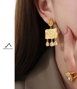 Detail of gold stainless steel rectangular earrings with wood grain texture and zircon drop