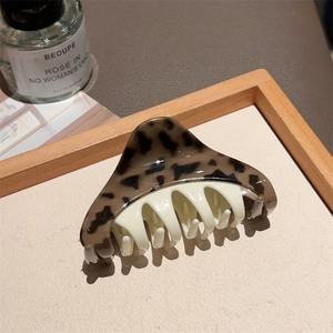 Detail of a leopard print and white acetate hair claw clip on a rustic wooden tray