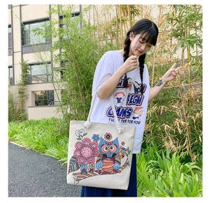 Detail of colorful owl embroidery and woven rope handles on a canvas tote bag