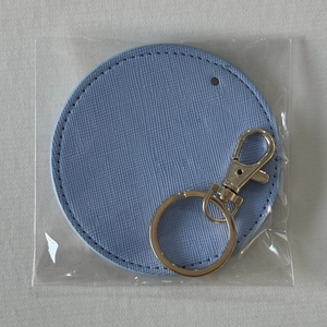 Close-up of a light blue round faux leather keychain with metal ring in plastic bag