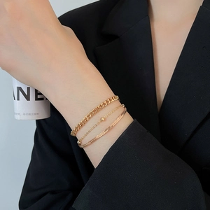 Detailed view of triple-layered golden metal snake chain and beaded bracelets on wrist