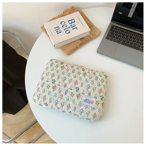 Close-up of quilted floral laptop sleeve in beige with a white Good Luck woven label