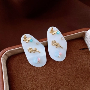 Detail of bamboo shell earrings with golden butterfly and rose motifs in a jewelry box
