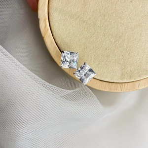Close-up of square-cut zircon stud earrings on a wood display with soft mesh backdrop
