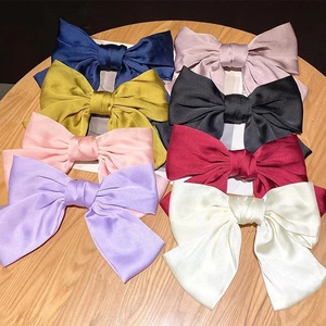 Set of eight large satin bow hair clips in various elegant colors on a wooden surface