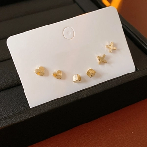 Close-up of golden earring set with heart, cube and X designs on display card