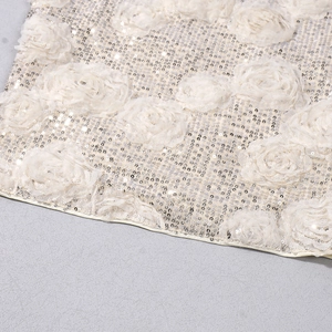 Detailed view of cream fabric featuring 3D rose appliqués and shiny sequin embroidery