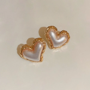 Elegant gold hammered heart stud earrings with faux pearl inlay on a beige background