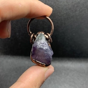 Dettaglio di un ciondolo in fluorite grezza fatto a mano con filo di rame avvolto