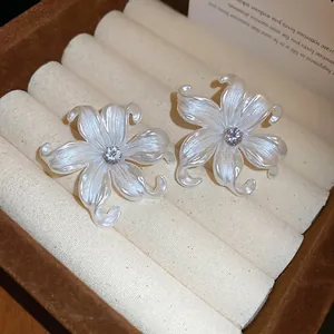 Elegant pearl white acrylic flower earrings with zircon center on a velvet display stand