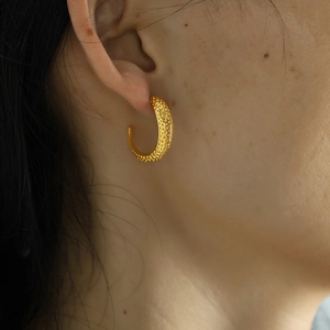 Golden moon texture C-shaped earrings with granular relief on a model's ear lobe