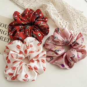 Close-up of three satin scrunchies with floral and cartoon prints on a lace surface