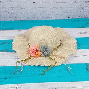 Close-up of beige woven straw sun hat with wavy brim and vibrant floral decorations