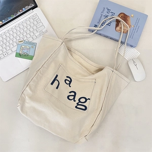 Detail of off-white canvas tote bag featuring a front pocket with haag letter print