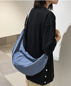 Détail d'un sac à bandoulière en nylon bleu porté par un mannequin dans un cadre épuré
