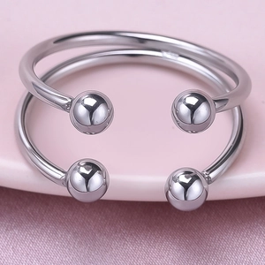 Vue détaillée de deux bagues ajustables en acier avec perles sur fond rose pastel