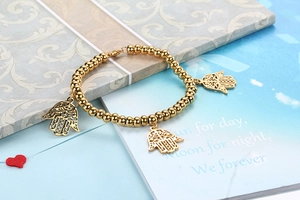 Detail showing gold bead elastic bracelet with hollow Hamsa Hand charms on card