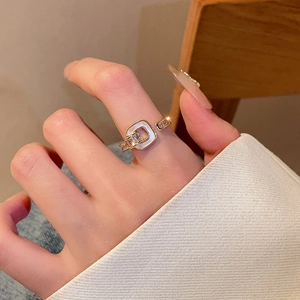 Close-up of gold square geometric ring with white enamel and zircon accents worn on hand
